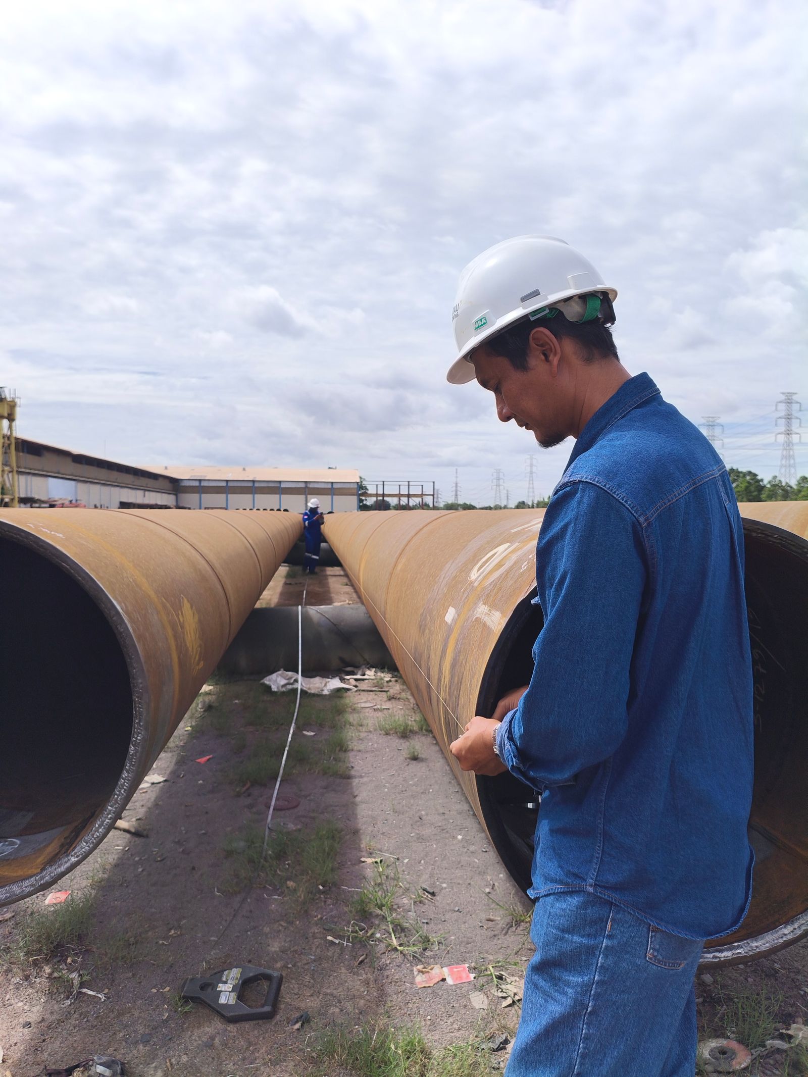 Worker beside a large-bore pipe section on a job site