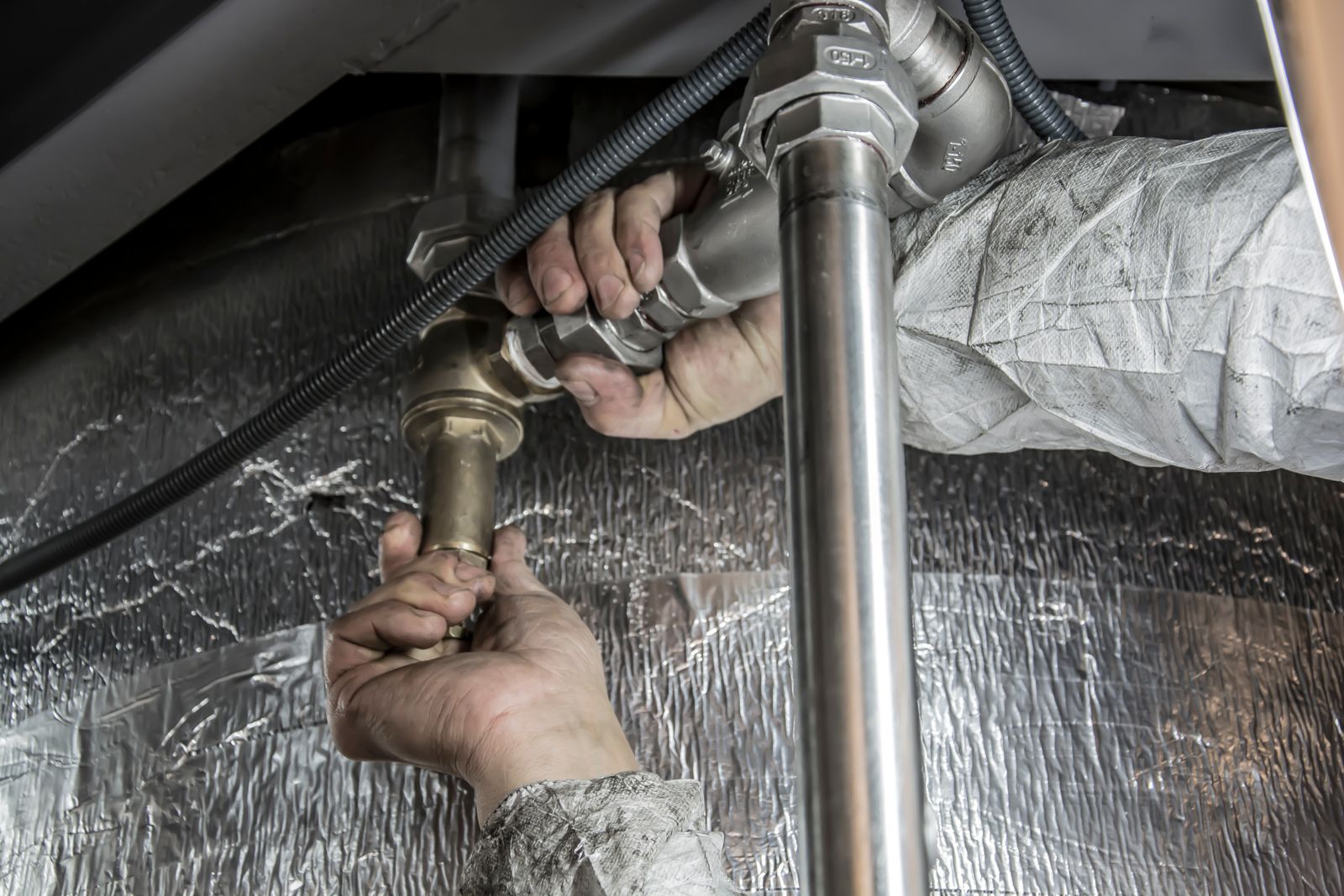Hands working on insulated pipe under a ceiling